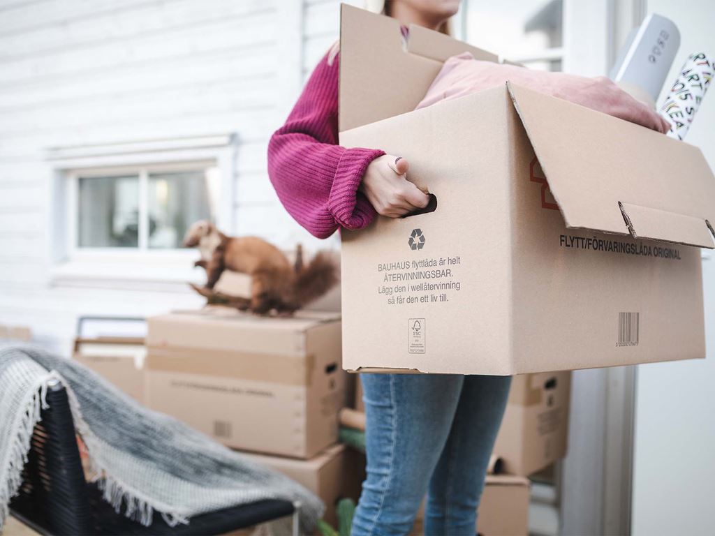 Kvinna bär flyttkartong till hennes nybyggda hus
