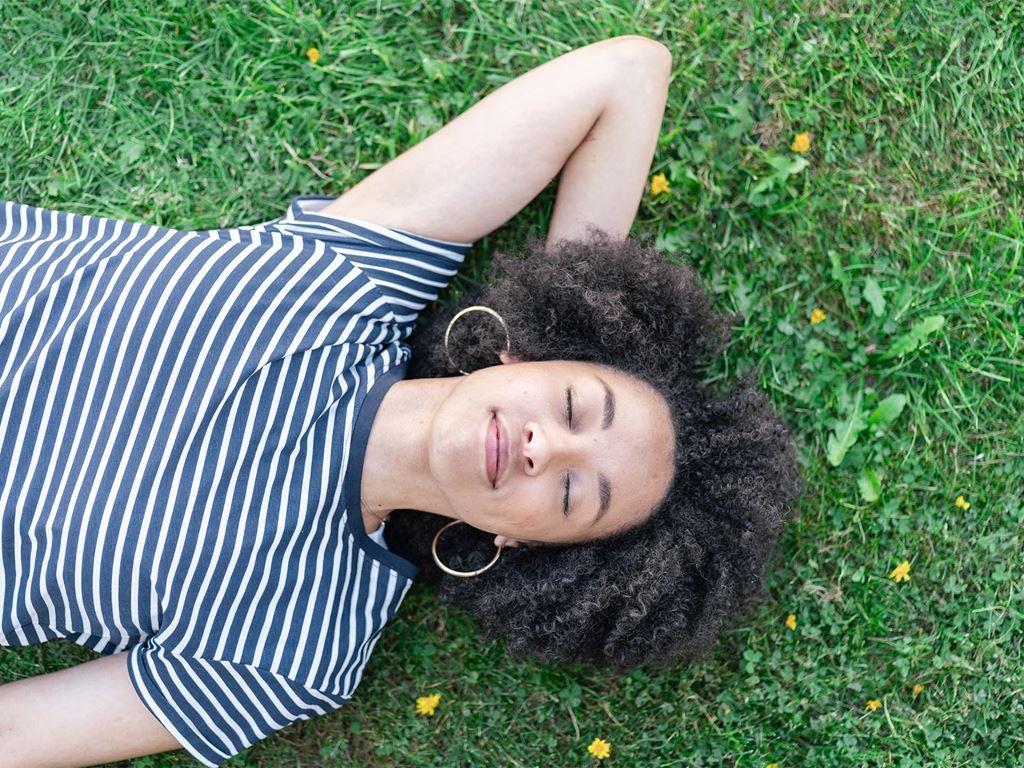 Kvinna ligger på gräsmatta och funderar över miljövänliga husalternativ