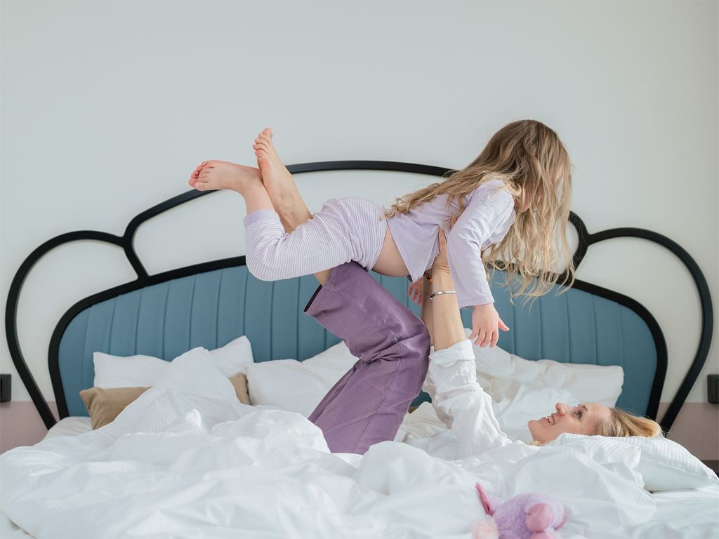 Kvinna lyfter barn i sängen på hotellrum