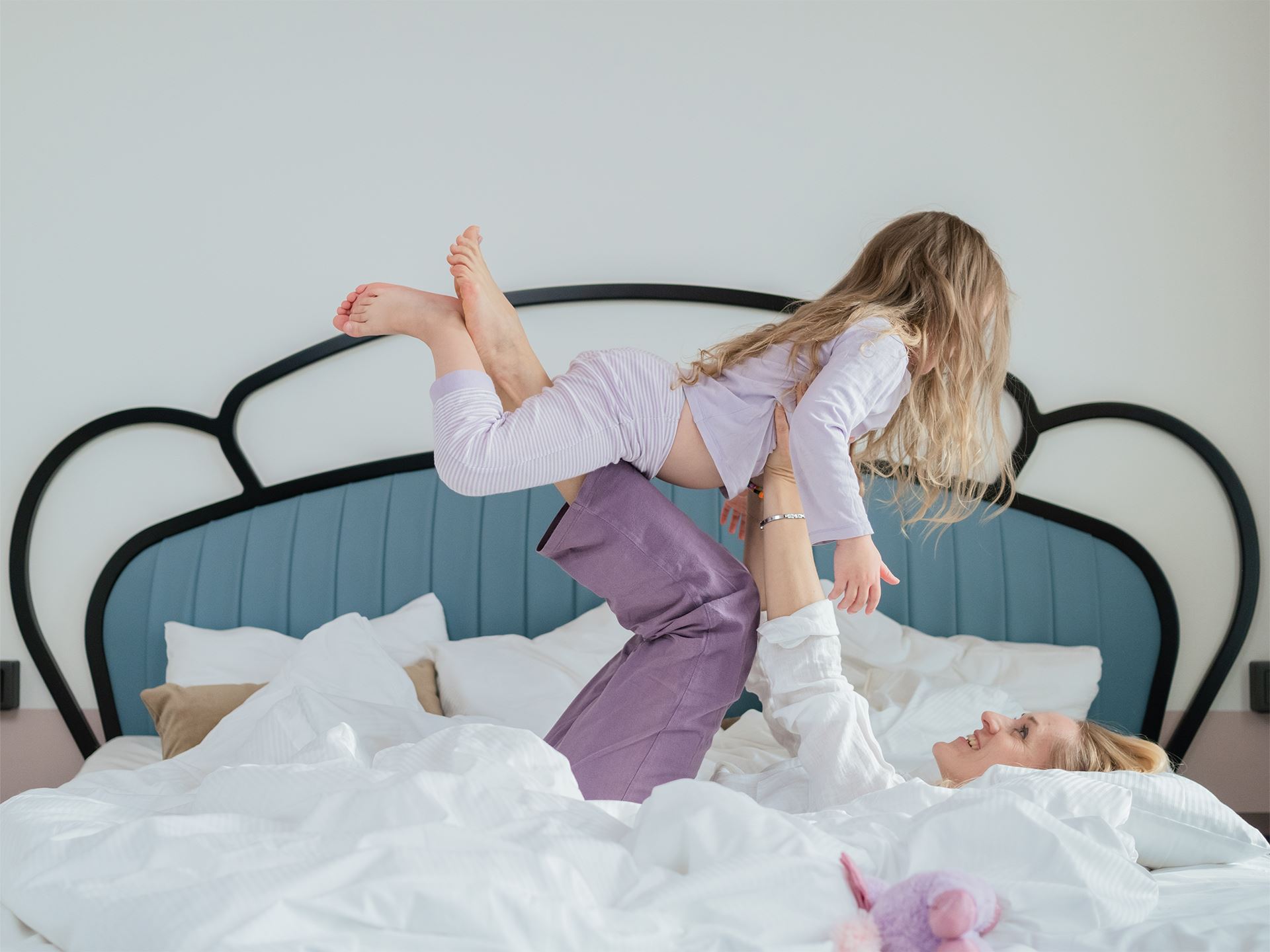 Kvinna lyfter barn i sängen på hotellrum